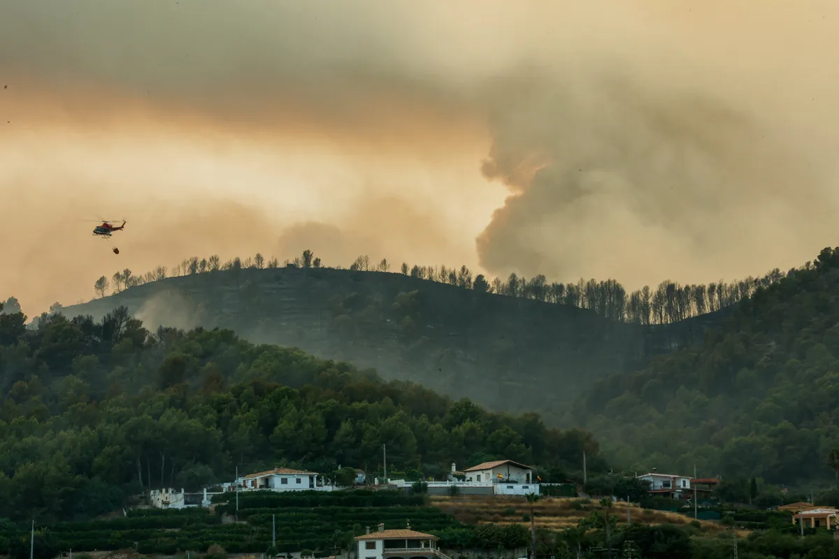 Ένα ελικόπτερο πετάει ενώ καπνός υψώνεται από τις πυρκαγιές στο Μπέτσι της Ισπανίας. REUTERS/Eva Manez